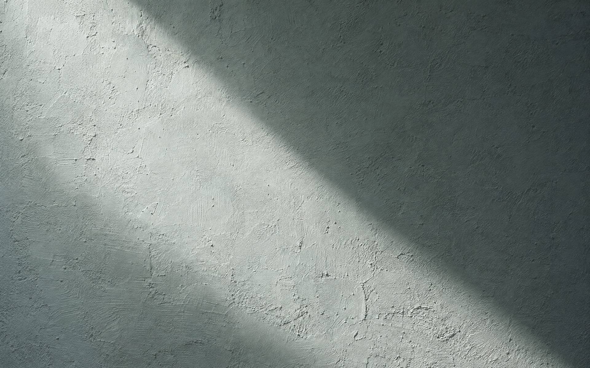Streifendes Licht fällt über eine unverputzte helle Wandfläche und macht die Oberfläche und kleine Unebenheiten sichtbar.